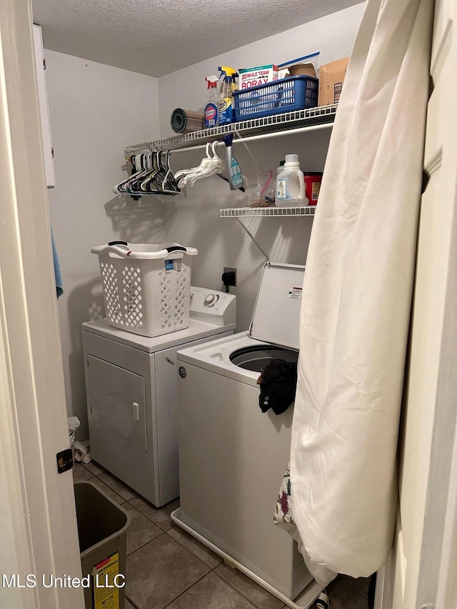 clothes washing area with a textured ceiling, washing machine and dryer, and tile patterned floors