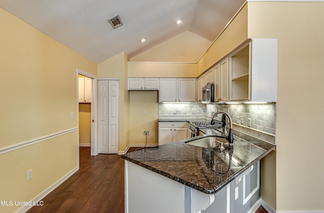 kitchen featuring visible vents, dark stone counters, appliances with stainless steel finishes, a peninsula, and a sink