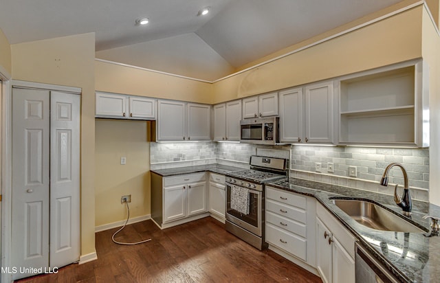 kitchen with dark wood-style floors, stainless steel appliances, lofted ceiling, a sink, and dark stone counters