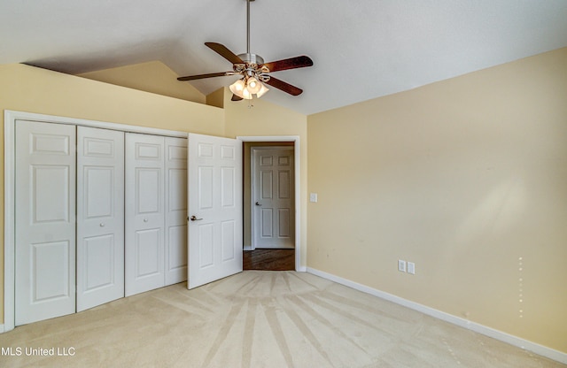 unfurnished bedroom with lofted ceiling, a closet, light colored carpet, ceiling fan, and baseboards