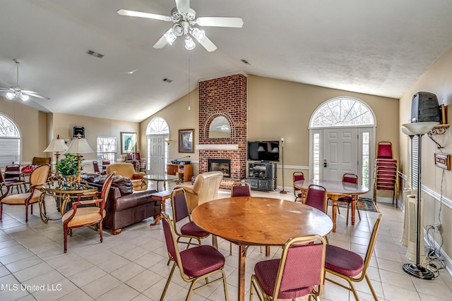 dining space with light tile patterned floors, high vaulted ceiling, visible vents, a ceiling fan, and a brick fireplace