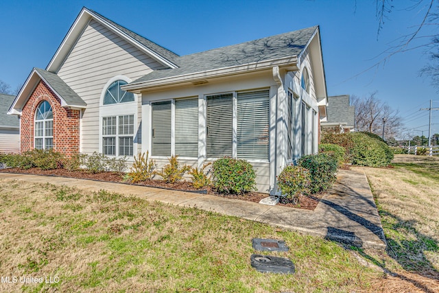 view of home's exterior featuring a yard, roof with shingles, and brick siding