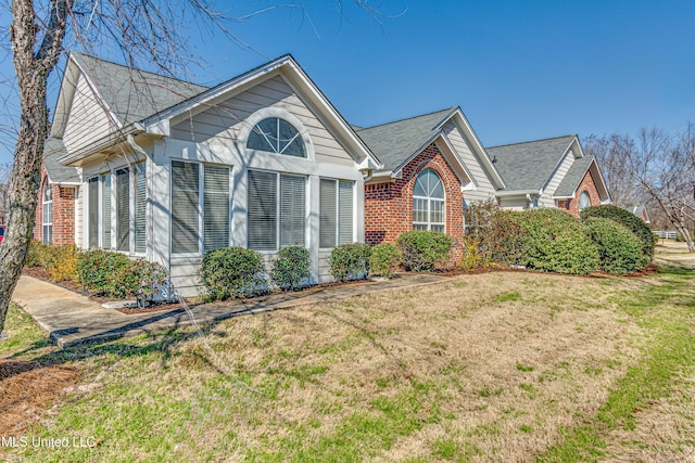 view of home's exterior with roof with shingles, brick siding, and a lawn