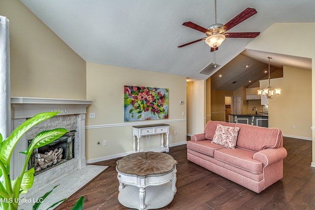 living room with lofted ceiling, ceiling fan with notable chandelier, dark wood-style flooring, a high end fireplace, and visible vents