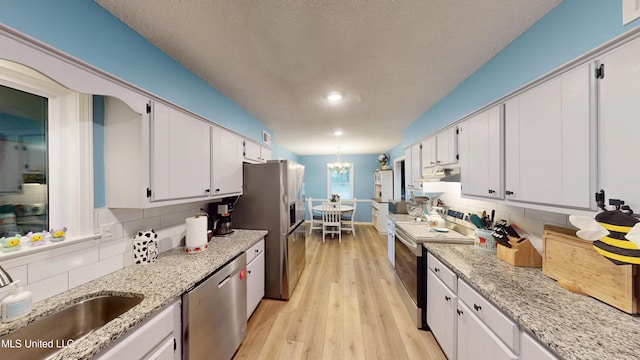 3902 S Windermere Dr, Nesbit, MS 38651 - kitchen with stainless steel appliances, backsplash, light wood-type flooring, white cabinets, and a chandelier