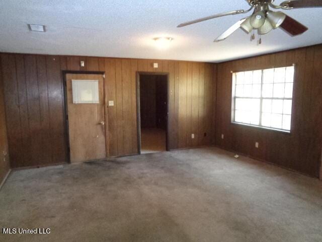 empty room with a textured ceiling, wood walls, ceiling fan, and carpet