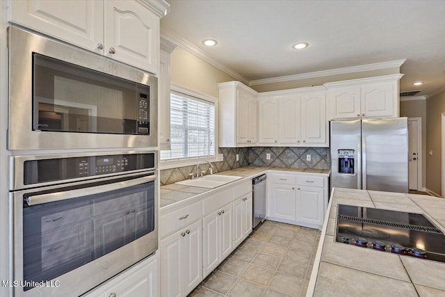 kitchen with stainless steel appliances, a sink, white cabinets, tile counters, and tasteful backsplash