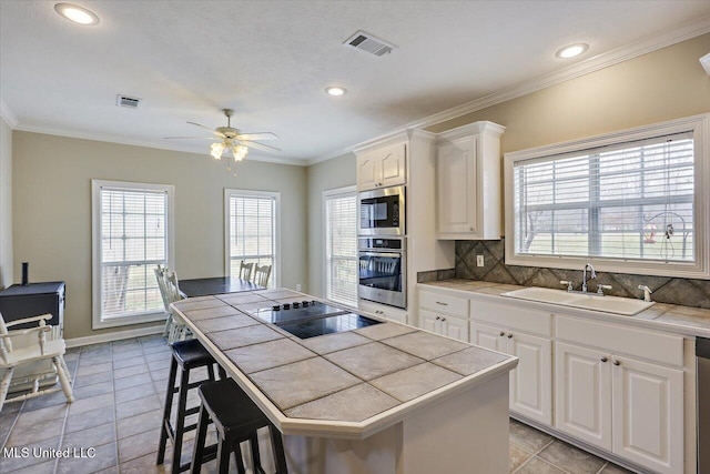 kitchen featuring tile countertops, stainless steel appliances, a sink, visible vents, and crown molding