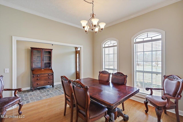 dining area featuring light wood-type flooring, crown molding, baseboards, and a notable chandelier