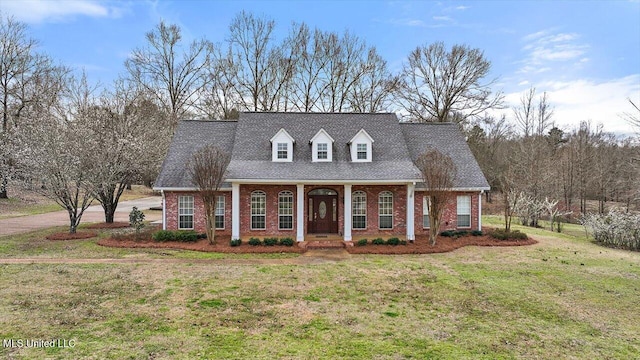 cape cod house with a shingled roof, a front yard, and brick siding