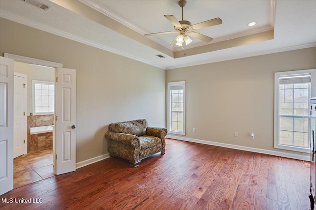 living area with ornamental molding, a raised ceiling, visible vents, and wood finished floors