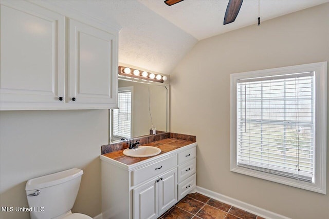 bathroom with lofted ceiling, toilet, ceiling fan, vanity, and baseboards