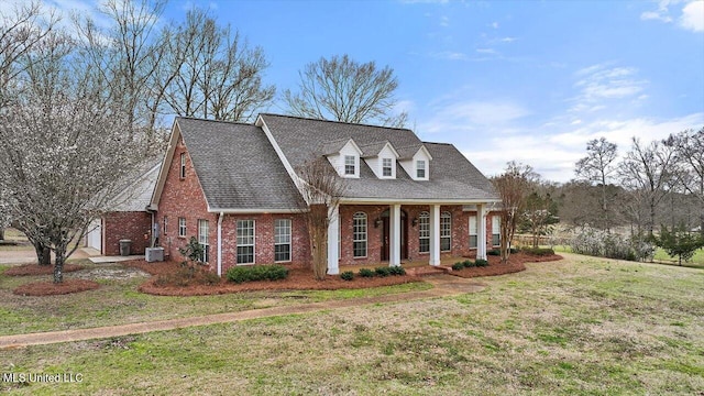 cape cod home featuring brick siding, a shingled roof, covered porch, cooling unit, and a front yard