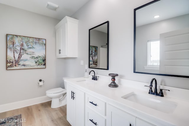 bathroom featuring double vanity, a sink, wood finished floors, and toilet
