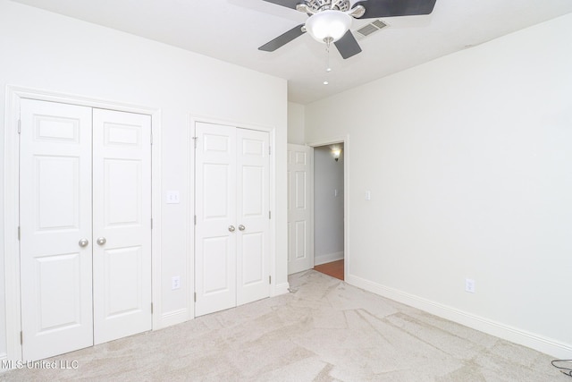 unfurnished bedroom featuring ceiling fan, light colored carpet, and two closets