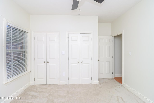 unfurnished bedroom featuring multiple closets, ceiling fan, and light colored carpet