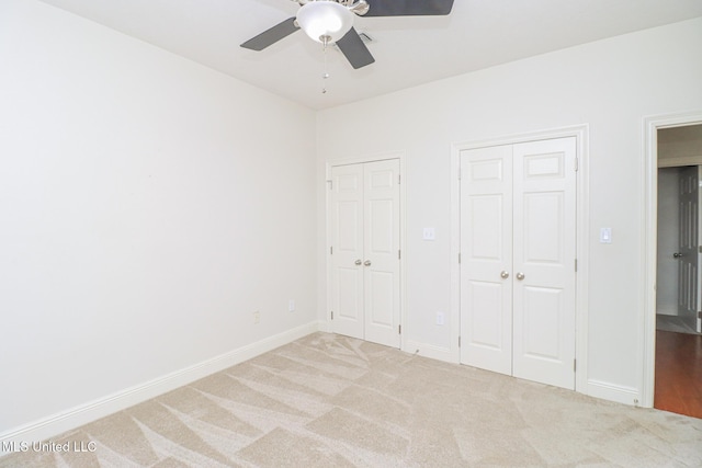 unfurnished bedroom featuring ceiling fan, light colored carpet, and multiple closets