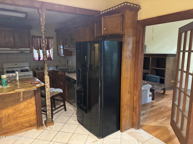 kitchen with black appliances, backsplash, dark brown cabinets, extractor fan, and light hardwood / wood-style flooring