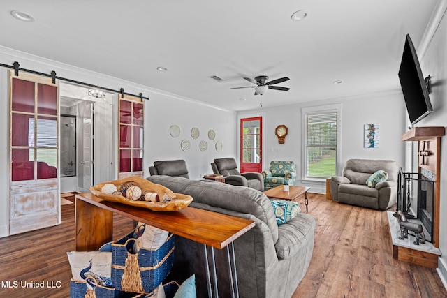 living room featuring ceiling fan, a barn door, crown molding, and hardwood / wood-style flooring