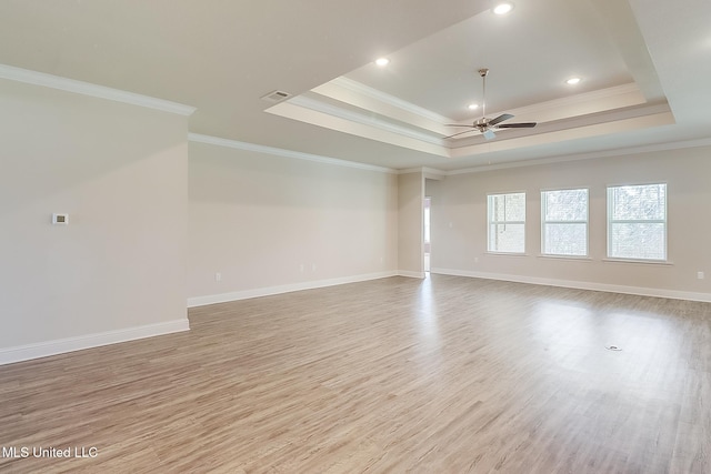 unfurnished room featuring ornamental molding, ceiling fan, light wood-type flooring, and a raised ceiling