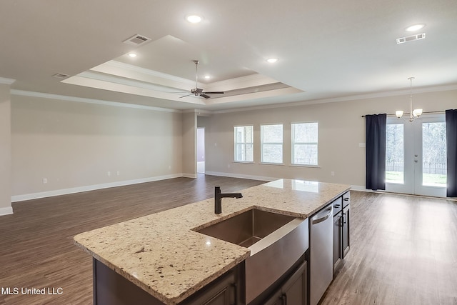 kitchen with an island with sink, light stone countertops, a tray ceiling, and stainless steel dishwasher