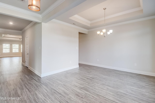 spare room with a tray ceiling, ornamental molding, an inviting chandelier, and hardwood / wood-style floors