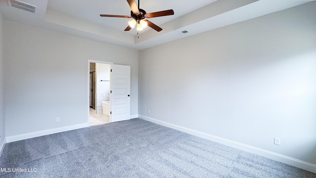 spare room featuring ceiling fan, a tray ceiling, and light carpet