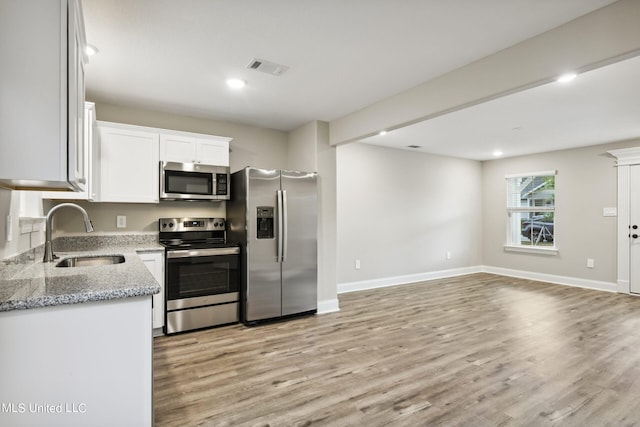 kitchen with sink, appliances with stainless steel finishes, light stone countertops, light hardwood / wood-style floors, and white cabinets