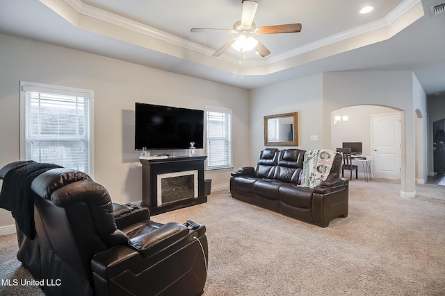 carpeted living room with a tray ceiling, crown molding, and ceiling fan with notable chandelier