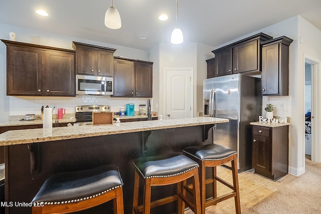 kitchen featuring decorative light fixtures, a kitchen bar, appliances with stainless steel finishes, and light hardwood / wood-style flooring