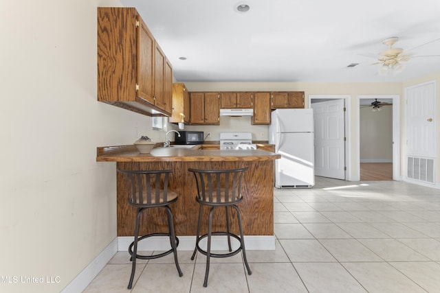 kitchen with visible vents, under cabinet range hood, freestanding refrigerator, a peninsula, and stove