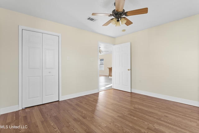 unfurnished bedroom featuring visible vents, baseboards, a closet, and wood finished floors