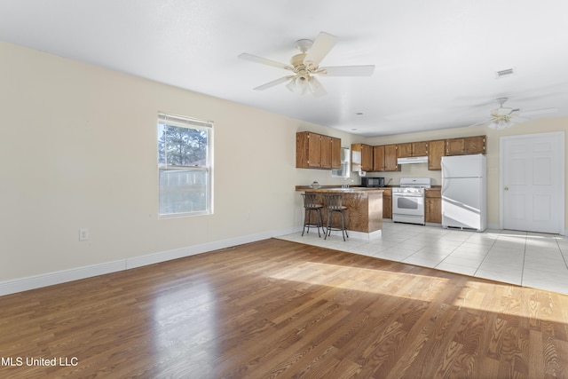 kitchen with visible vents, white appliances, a peninsula, brown cabinetry, and light wood finished floors