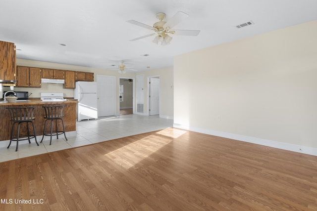 kitchen with visible vents, under cabinet range hood, white appliances, a peninsula, and brown cabinetry