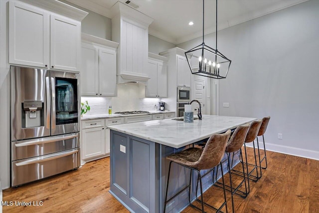 kitchen featuring a kitchen island with sink, white cabinets, light stone counters, and appliances with stainless steel finishes