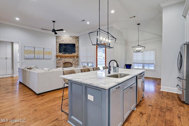 kitchen with sink, decorative light fixtures, a fireplace, a center island with sink, and appliances with stainless steel finishes