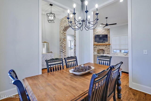 dining space with ornamental molding, brick wall, ceiling fan, wood-type flooring, and a fireplace