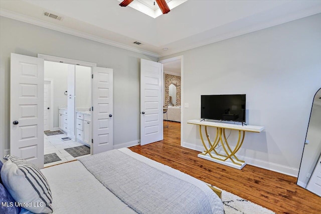 bedroom featuring ceiling fan, light wood-type flooring, crown molding, and connected bathroom