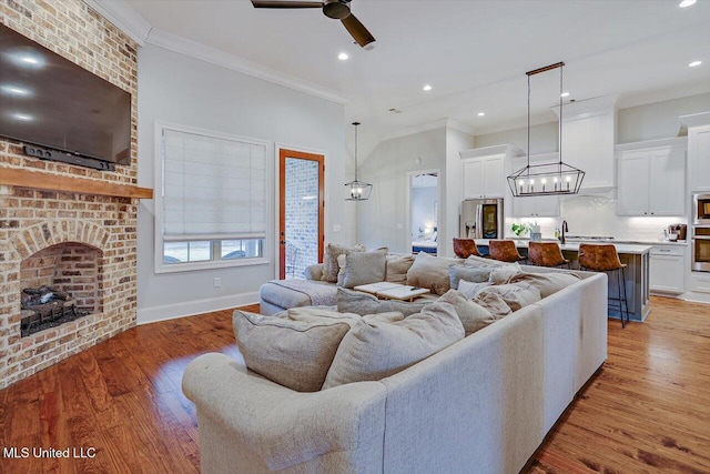 living room with ornamental molding, ceiling fan, sink, light hardwood / wood-style flooring, and a fireplace