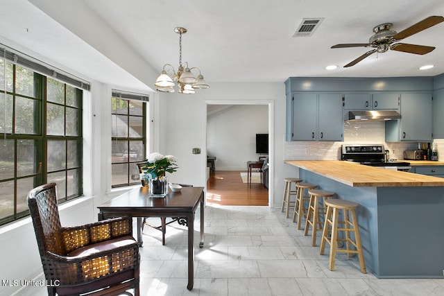 kitchen with backsplash, stainless steel electric range oven, butcher block counters, ceiling fan with notable chandelier, and decorative light fixtures