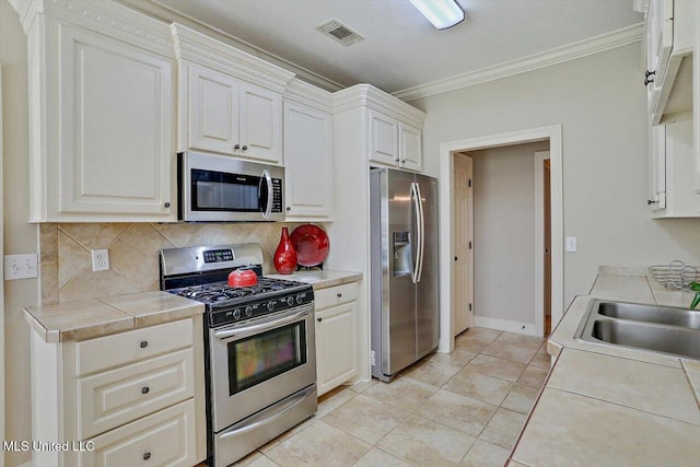 kitchen featuring ornamental molding, stainless steel appliances, light tile patterned floors, tile countertops, and white cabinets