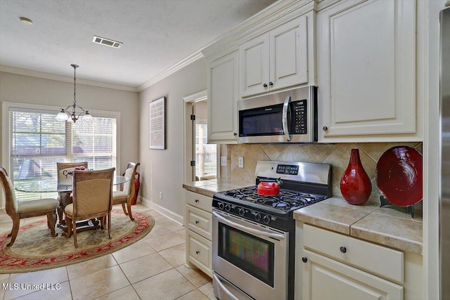 kitchen with an inviting chandelier, backsplash, appliances with stainless steel finishes, light tile patterned floors, and ornamental molding