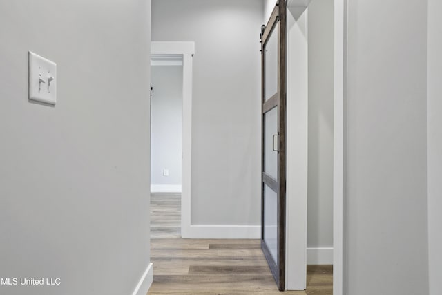 hall with a barn door, wood finished floors, and baseboards