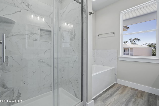 bathroom with a marble finish shower, wood finished floors, baseboards, and a bath