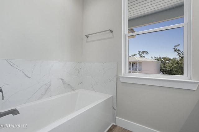 full bath featuring plenty of natural light, a bath, baseboards, and wood finished floors