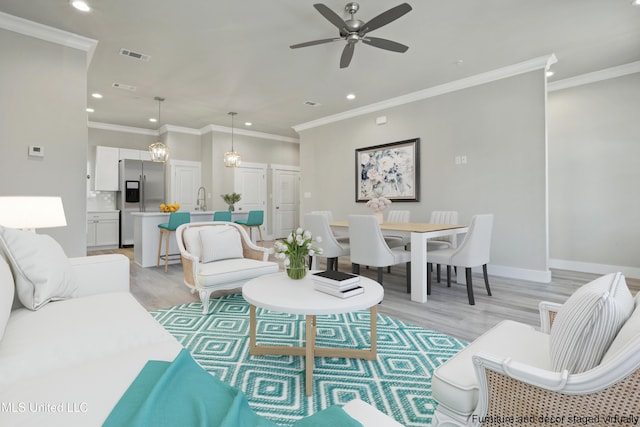 living room with light wood finished floors, recessed lighting, a ceiling fan, ornamental molding, and baseboards