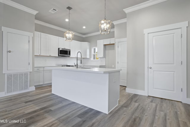 kitchen featuring stainless steel microwave, ornamental molding, white cabinetry, light wood-style floors, and a center island with sink