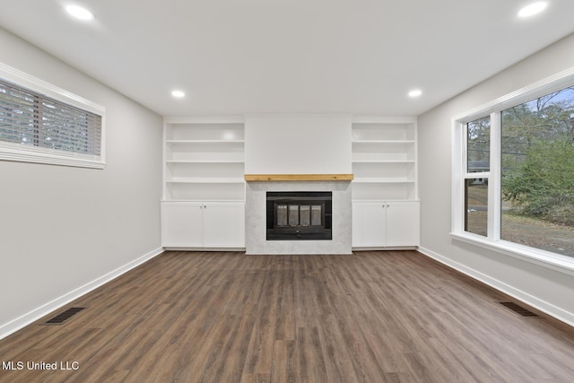 unfurnished living room featuring built in shelves, a fireplace, and dark hardwood / wood-style flooring