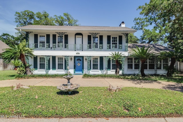 colonial-style house with covered porch, a chimney, and a front yard
