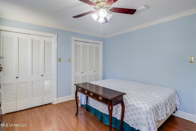 bedroom featuring a ceiling fan, baseboards, ornamental molding, wood finished floors, and multiple closets